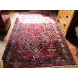 A Middle Eastern-style red-ground hand knotted wool rug with multicoloured isometric designs with
