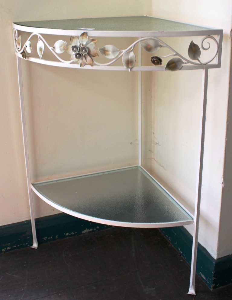 A mid 20th century white-painted metal corner table with glass top, shelf under, with floral and