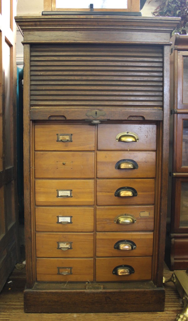 An early 20th century oak stained office reference bureau with shaped cornice, rolled down tambour-