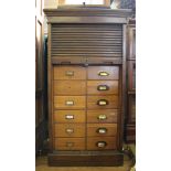An early 20th century oak stained office reference bureau with shaped cornice, rolled down tambour-