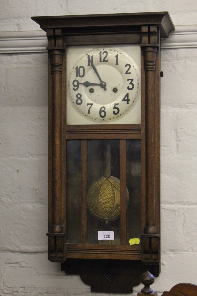 An early 20th century oak framed wall clock with shaped cornice, column supports, circular dial with