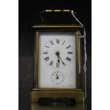 A vintage brass carriage clock with Roman numerals on a shaped base with handle