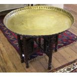 A large Indian brass tray on folding wood stand, 62cm diameter