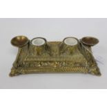 AN OLD CAST BRASS DOUBLE INK WELL with scrolling foliate decoration standing on four feet, 27cm