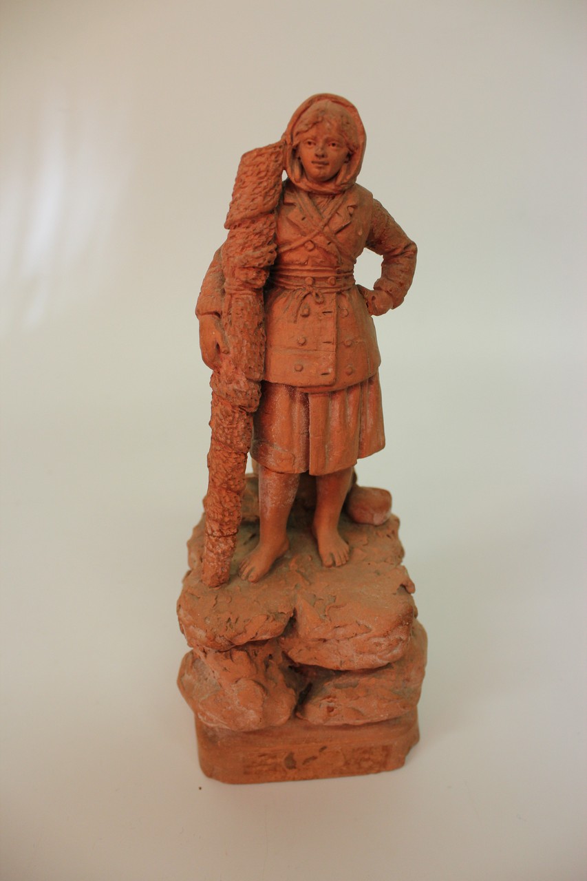 A LATE 19TH/EARLY 20TH CENTURY BRETON TERRACOTTA FIGURE of a woman standing on a rocky outcrop,