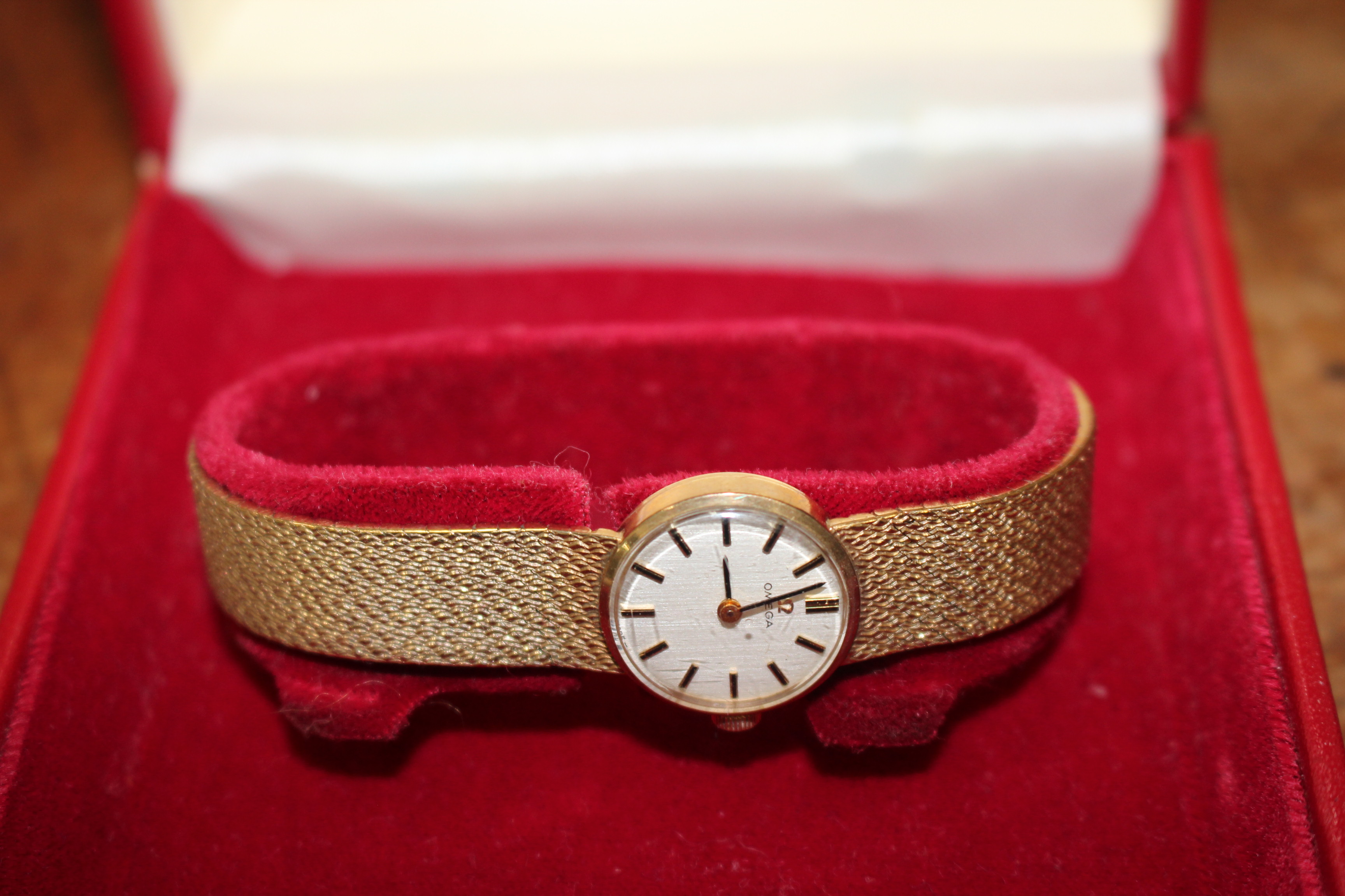 A 9-CARAT GOLD OMEGA WRISTWATCH with textured strap, silvered dial and baton numeral markings