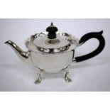 A SMALL SILVER BACHELORS TEA POT with a shaped rim and standing on short hoof feet with sea scroll