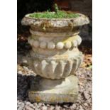 A CARVED STONE URN of cylindrical form with fluted base and square stand, 43cm diameter x 54cm high