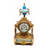 A GILT METAL AND PORCELAIN MOUNTED MANTLE CLOCK, the case with lion mask and laurel wreath ring