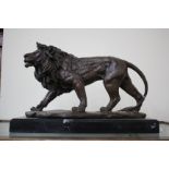 A MODERN BRONZE SCULPTURE OF A LION walking along, the sculpture mounted on a rectangular stone