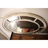 A CREAM PAINTED OVAL WALL MIRROR, the central plate with further radiating small plates surrounding,