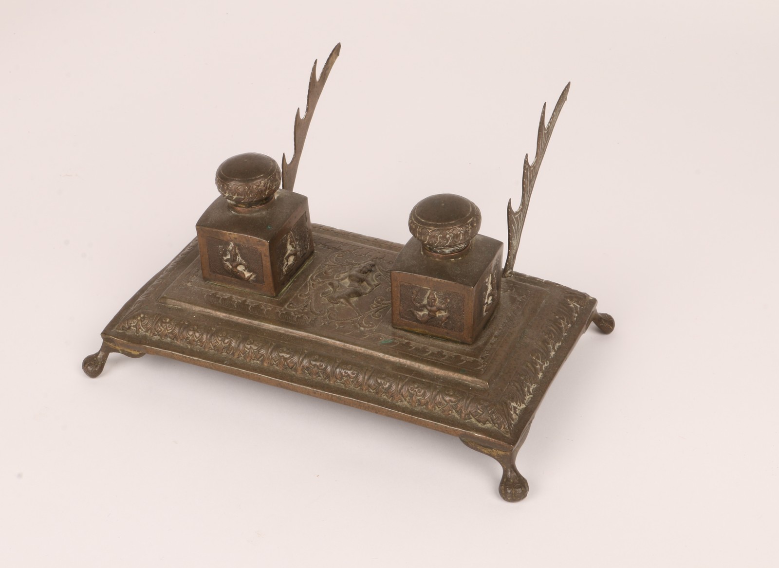 AN INDIAN SILVER COLOURED METAL DESK STAND with twin inkwells and dancing figure decoration, 19cm