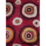 A MIDDLE EASTERN DARK RED GROUND BED COVER with polychrome stylised flower head decoration,