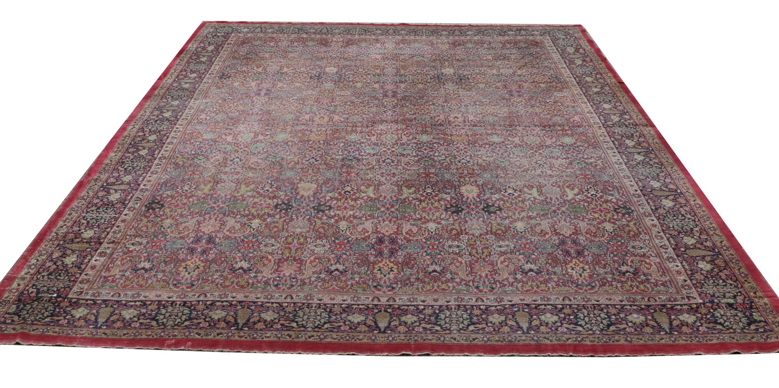 AN OLD KIRMAN LARGE RED GROUND CARPET with repeating polychrome foliate decoration within a multiple