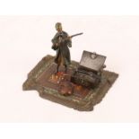 AN AUSTRIAN COLD CAST BRONZE MODEL of a man examining a chest of weapons and standing on a carpet,