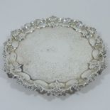 An ornate Victorian silver salver, of circular shape with a piecrust border on three scrolled feet,