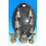 A ring of 7 brass bells on ebonised wall plaque; a pair of brass candlesticks