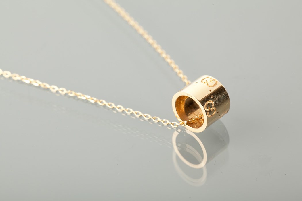 EIGHTEEN CARAT GOLD GUCCI PENDANT ON CHAIN of cylindrical form, with engraved G motifs and dotted