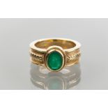 EMERALD RING
set with an oval cut emerald, on a wide band with ornate detailing to shoulders,