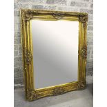 A MOULDED GILT WALL MIRROR,
O.R.M, the ornate swept frame, around a bevelled plate, 61.