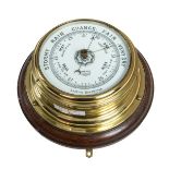 A BRASS CASED SHIPS ANEROID BAROMETER, 
by Gamage of London, mounted on an oak panel, 10in (26cm).