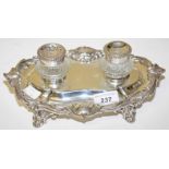 A SILVER PLATED DESK STAND, 
with two cut glass jars, on Rococo style stand and shell scroll legs,