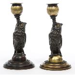 A PAIR OF BRONZE AND GILT BRONZE CANDLE STICKS, 
each modelled as an owl perched on a sphere,