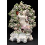 A DERBY FIGURAL CANDLESTICK OF CUPID  in flowered drapery and kneeling on a mound before bocage