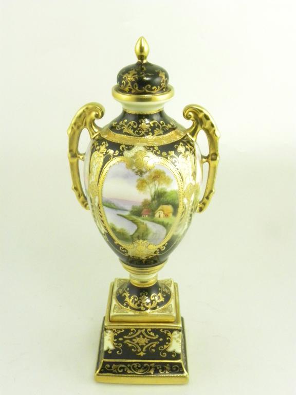 A NORITAKE BLACK GROUND TWO HANDLED OVIFORM VASE AND COVER, PAINTED WITH FOUR OVAL LANDSCAPE PANELS