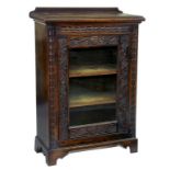 A DARK STAINED AND CARVED OAK CABINET WITH GLAZED DOOR