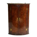 A GEORGE III OAK AND CROSSBANDED BOW FRONTED CORNER CUPBOARD