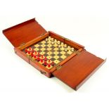 A VICTORIAN MAHOGANY TRAVELLING CHESS BOARD CONTAINING A SET OF CONTEMPORARY MINIATURE BONE CHESS