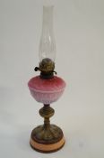 A brass oil lamp with pink glass shade