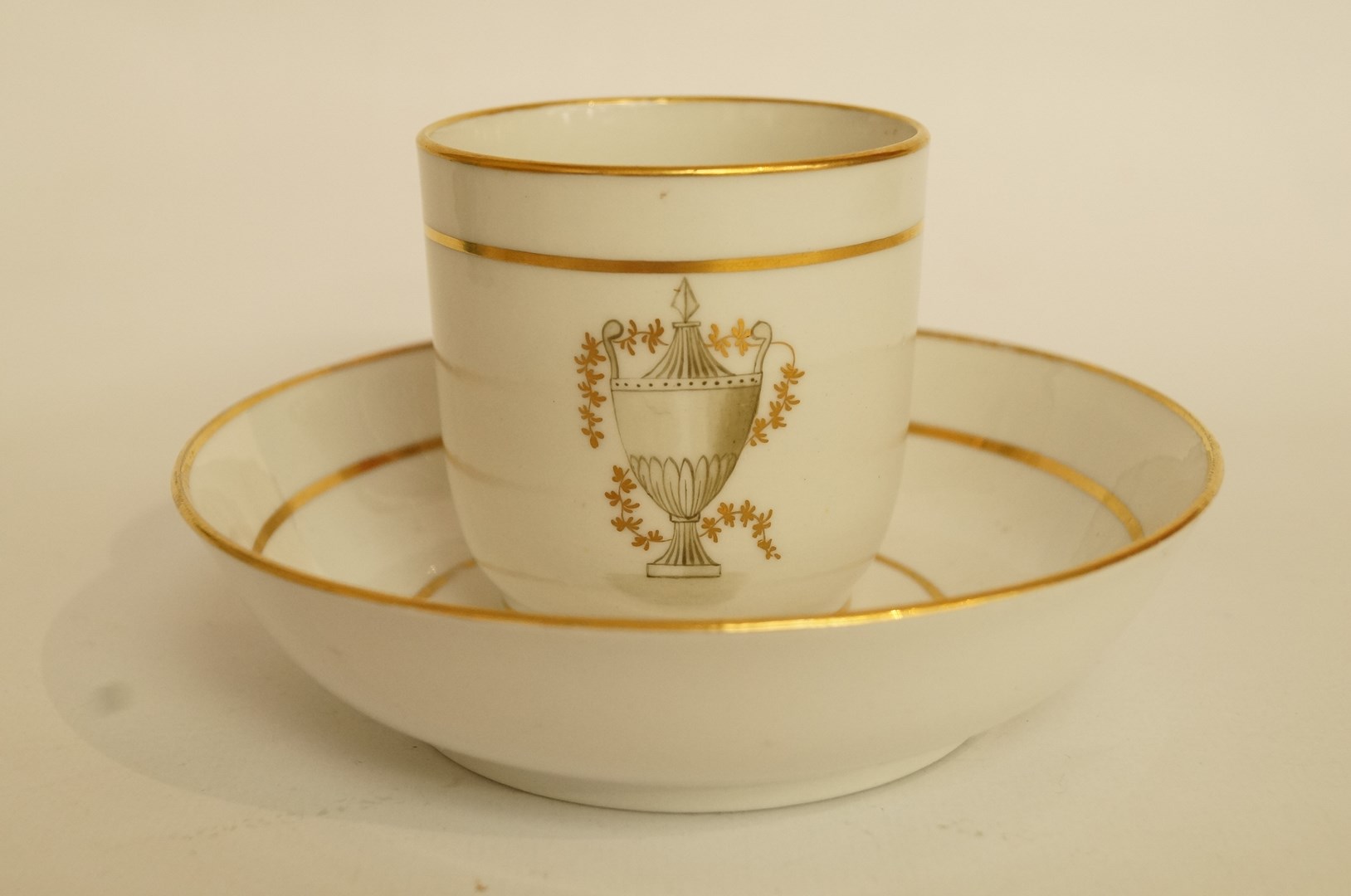 A Factory Z porcelain coffee cup and saucer, painted engrise with an urn within gilt line bands