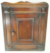 A 19th century oak hanging corner cabinet the panelled door opening to reveal two shelves,