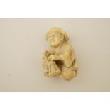 An early 20th century ivory netsuke man kneeling and playing a bongo drum,