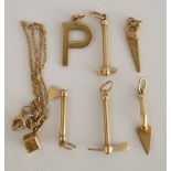 A collection of five 9 carat gold charms in the form of a saw, hammer, pick axe,