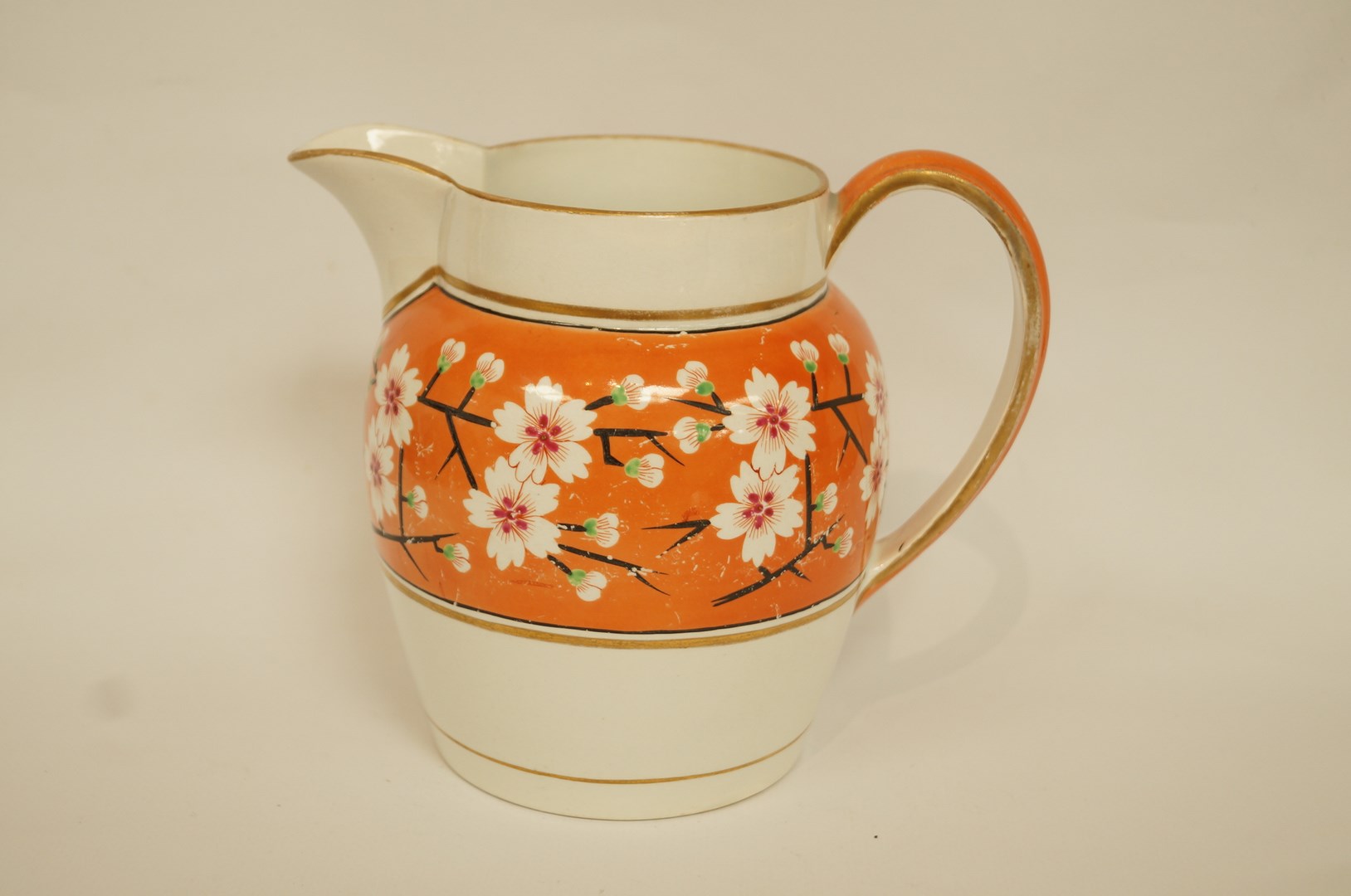 A Wedgwood pearlware jug painted with prunus on an orange ground within gilt line borders,