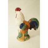 A tin glazed pottery figure of a cockerel, moulded standing on an integrated oval base,