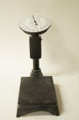 A painted black weighing machine with a white enamel face,