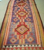 A large Kelim rug with three joined medallions on a purple field within multiple boarders,
