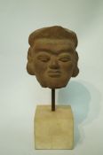 A Burmese terracotta model of a head mounted on a plinth,