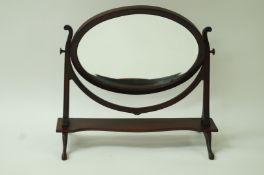 An Edwardian mahogany swing frame mirror with oval bevelled mirror plate,
