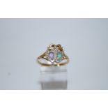 An amethyst, emerald and diamond 9 carat gold lovers hearts ring, with a ribbon bow surmount,