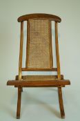 An 19th century colonial folding chair with caned seat and back and curved out swept legs