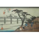 A 20th century Japanese woodblock print of figures on the riverbank with a bridge beyond, p.