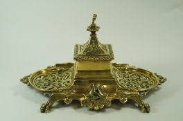 A Victorian brass desk stand, with central inkwell, pierced sides and dual pen rests, on claw feet,