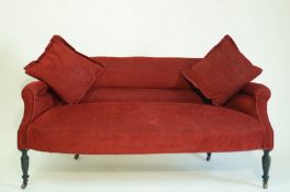 An Edwardian two seat sofa with low back, on turned ebonised legs with brass and ceramic casters,