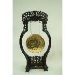 An early 20th Chinese carved hardwood gong stand suspending a brass gong,