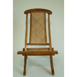 An 19th century colonial folding chair with caned seat and back and curved out swept legs